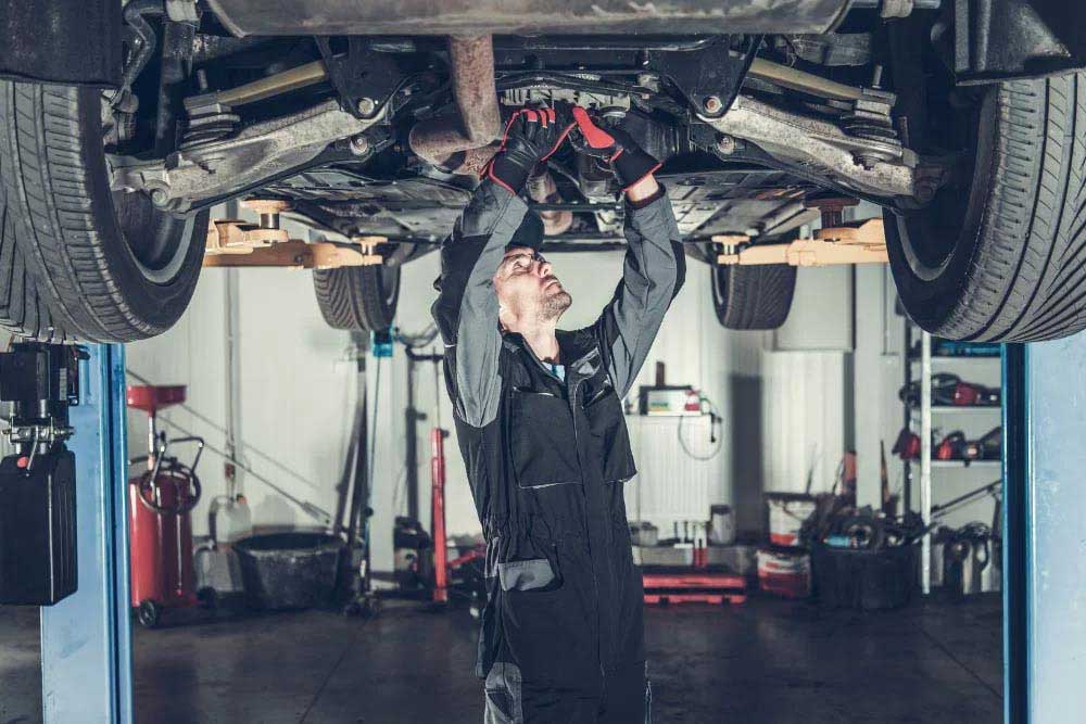 A mechanic working under a car which is lifted.